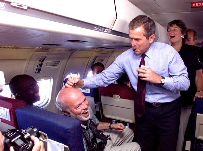 Gov. George W. Bush of Texas, signs the head of Newsweek photographer David Hume Kennerly during the flight to launch his presidential campaign in Cedar Rapids, Iowa.