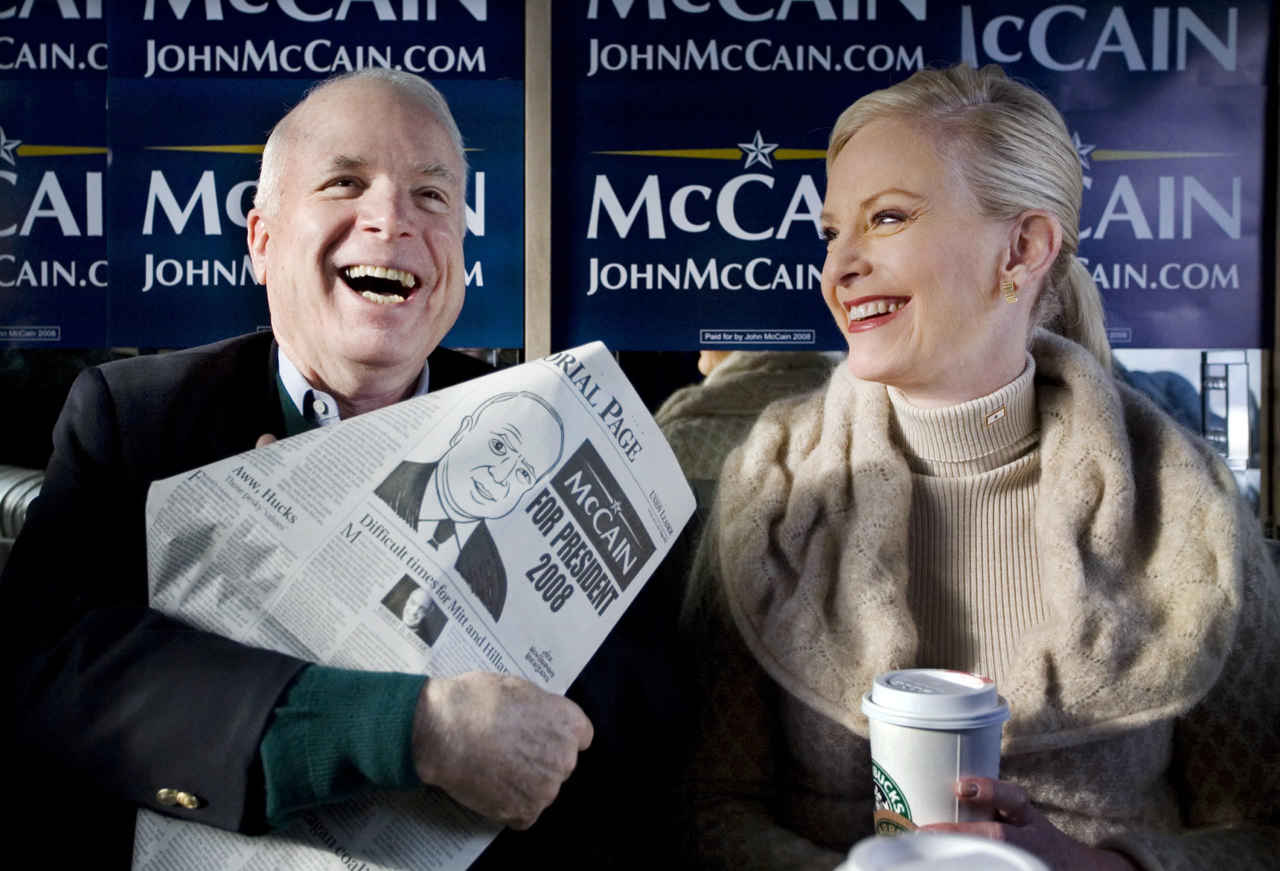 On election day in New Hampshire, Republican Presidential contender Senator John McCain shows reporters the editorial page of the Manchester Union Leader which features a cartoon of him.  His wife Cindy McCain sits beside him on their campaign bus, "The Straight Talk Express,"  Nashua, New Hampshire, January 8, 2008.