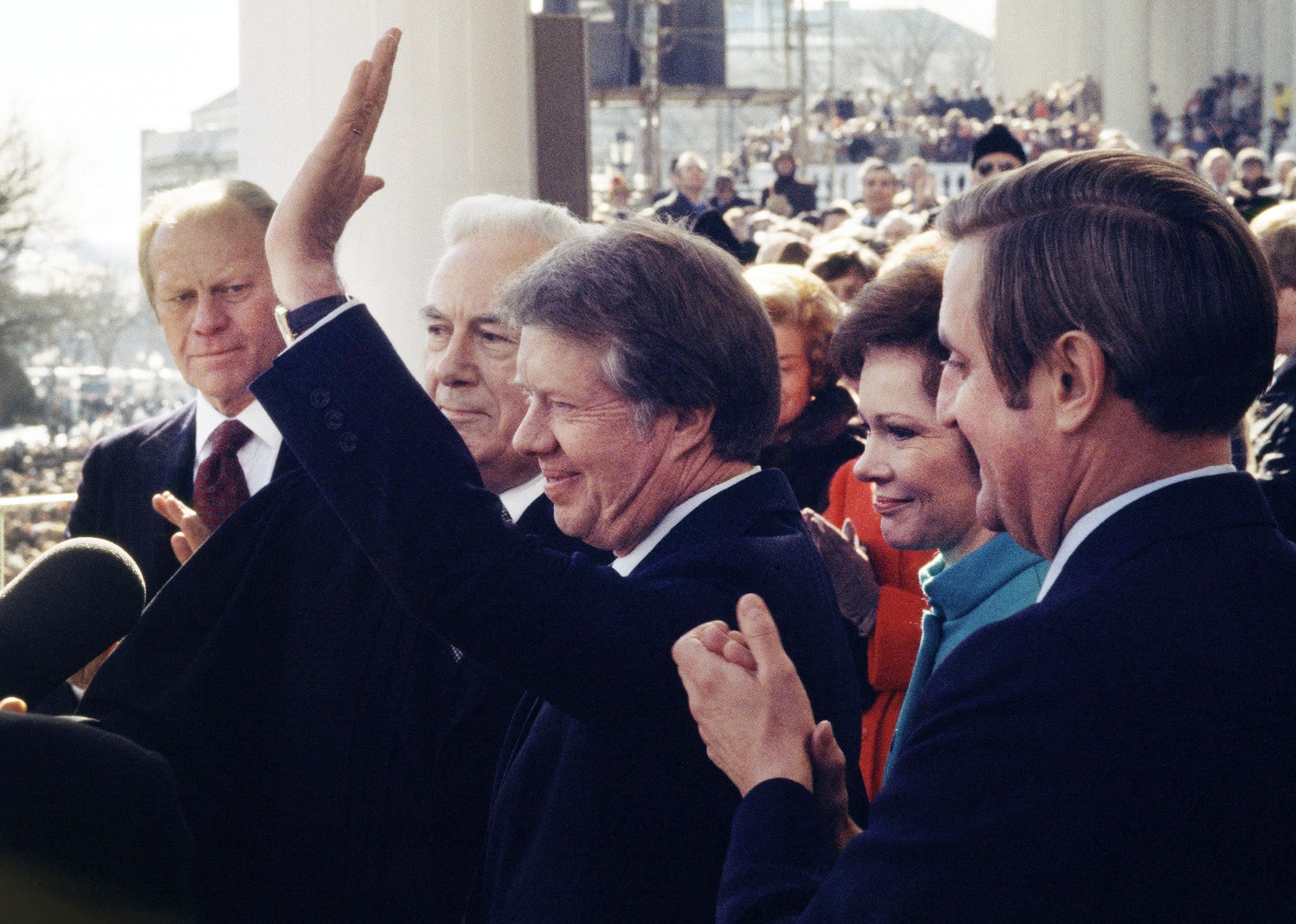 President Jimmy Carter after his swearing in as Chief Justice Warren Burger and former President Ford watch him wave to the crowd